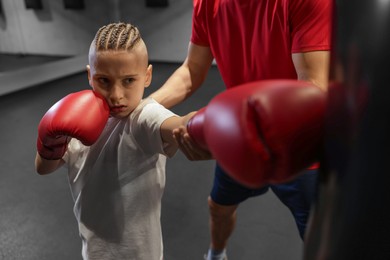 Photo of Boy in protective gloves with his boxing coach at training center