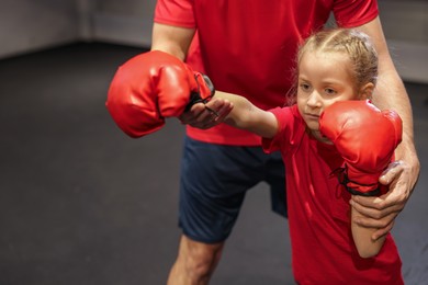 Photo of Girl in protective gloves having boxing practice with her coach at training center