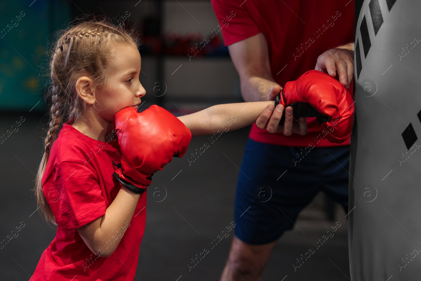 Photo of Girl in protective gloves having boxing practice with her coach at training center