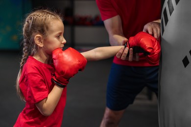 Photo of Girl in protective gloves having boxing practice with her coach at training center