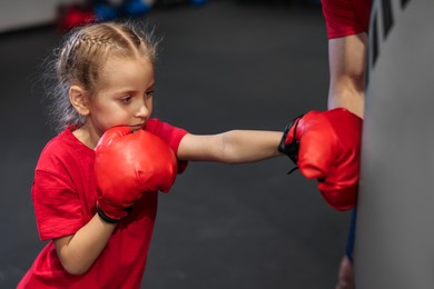 Photo of Girl in protective gloves having boxing practice with her coach at training center