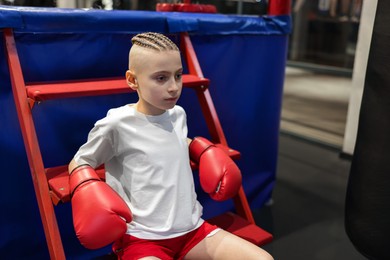 Photo of Boy in protective gloves sitting near boxing ring