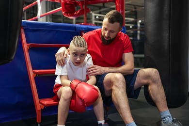 Photo of Coach comforting sad boy near boxing ring