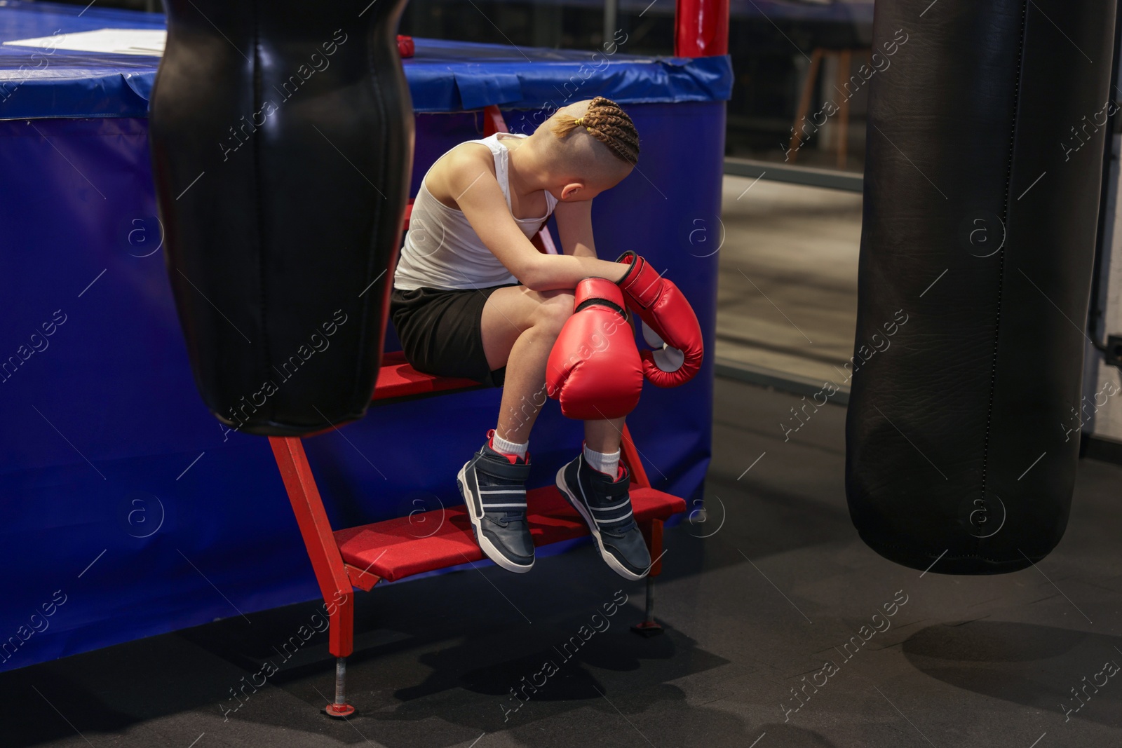 Photo of Sad boy in protective gloves near boxing ring indoors