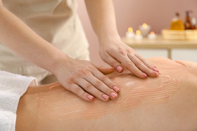 Esthetician applying cosmetic product for body wraps treatment onto woman's back in spa salon, closeup