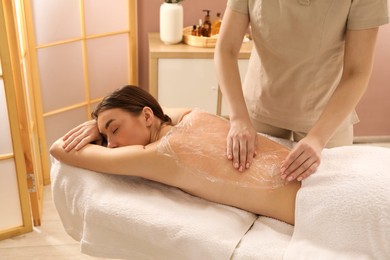 Woman undergoing body wraps treatment in spa salon