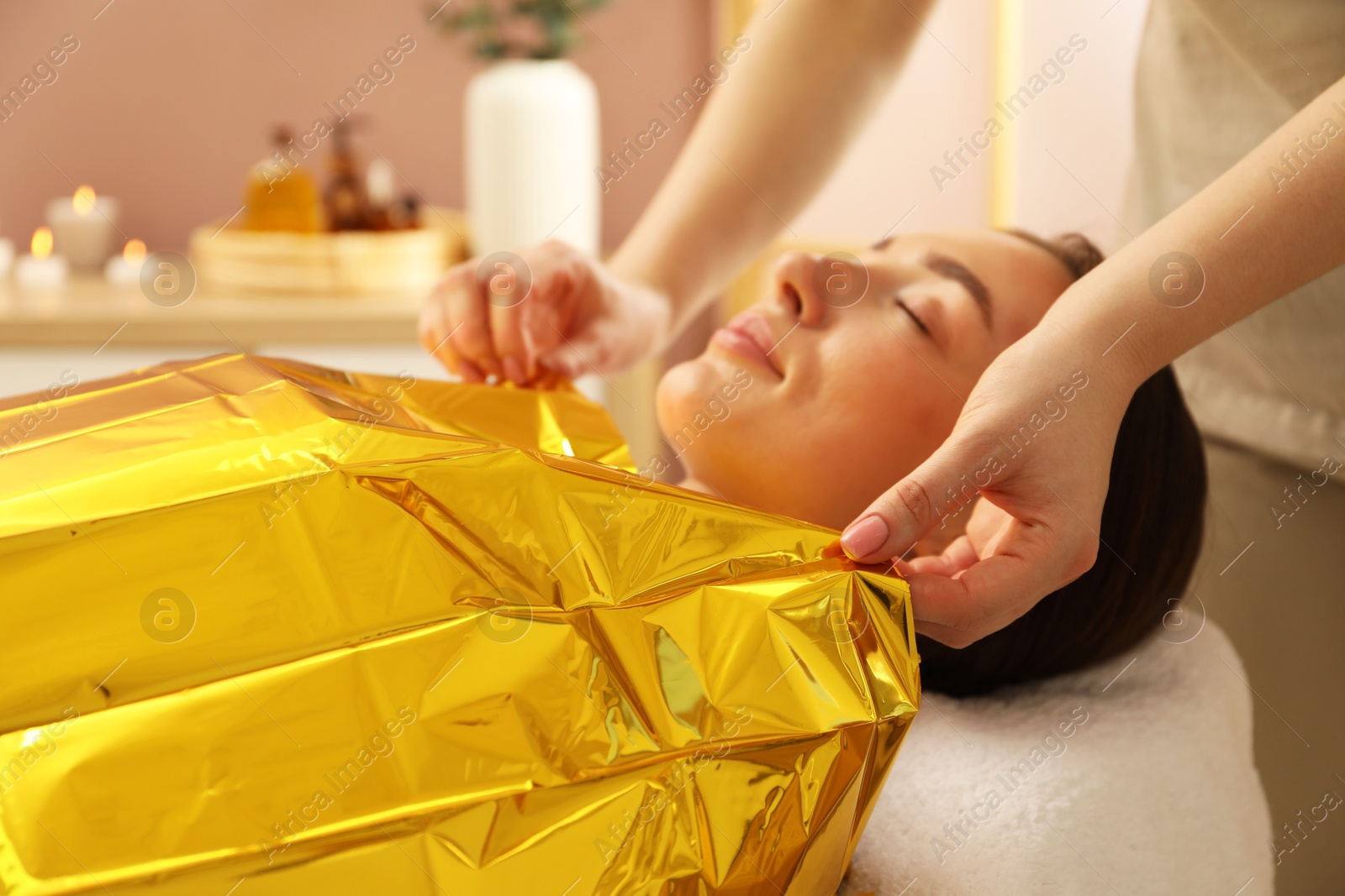 Photo of Spa body wraps. Esthetician covering woman with thermal foil blanket indoors, closeup