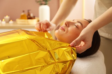 Spa body wraps. Esthetician covering woman with thermal foil blanket indoors, closeup