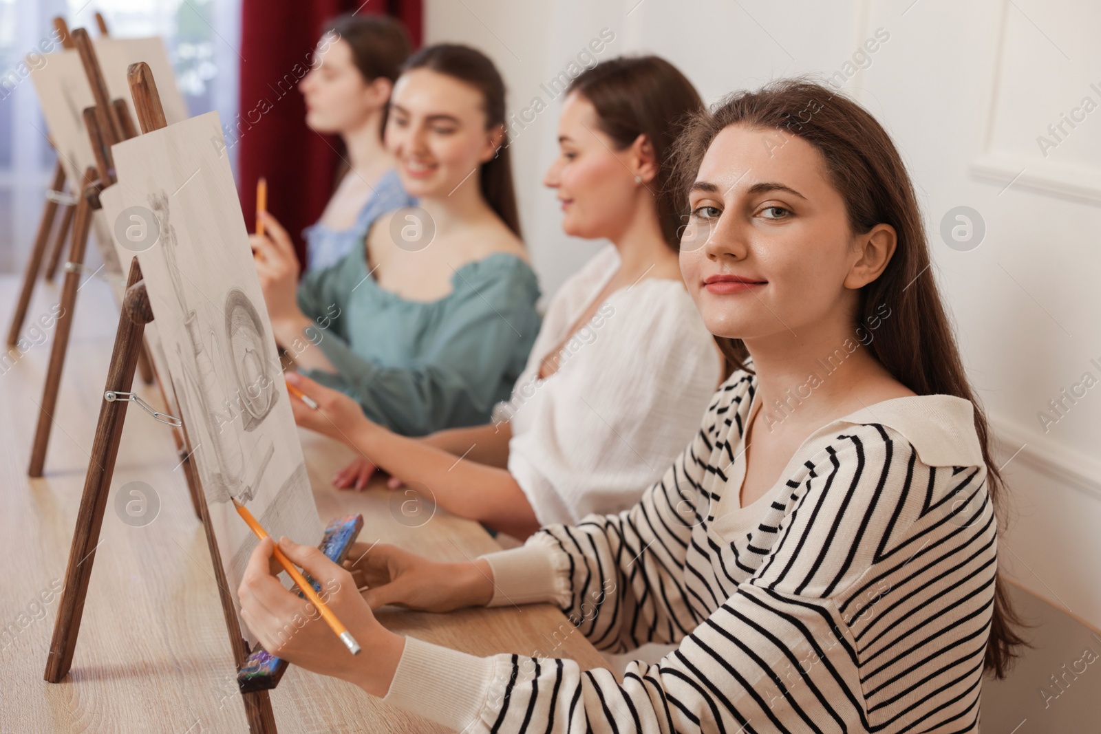 Photo of Group of women with easels learning to draw at wooden table in class