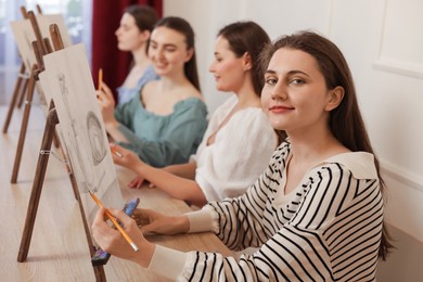 Group of women with easels learning to draw at wooden table in class