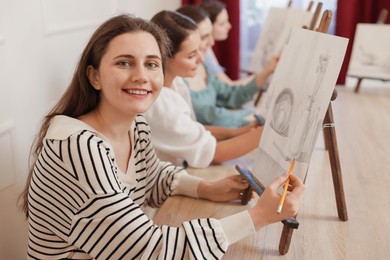 Group of women with easels learning to draw at wooden table in class