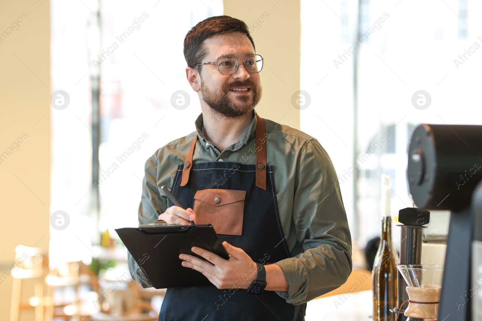 Photo of Smiling business owner working with clipboard in his cafe