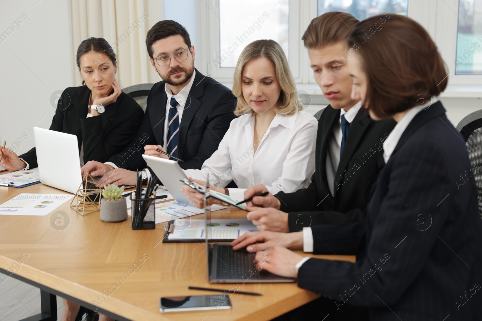 Photo of Coworkers with different devices working together at wooden table in office