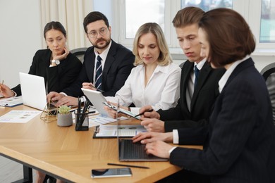 Coworkers with different devices working together at wooden table in office