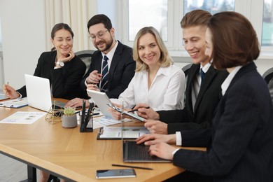 Coworkers with different devices working together at wooden table in office