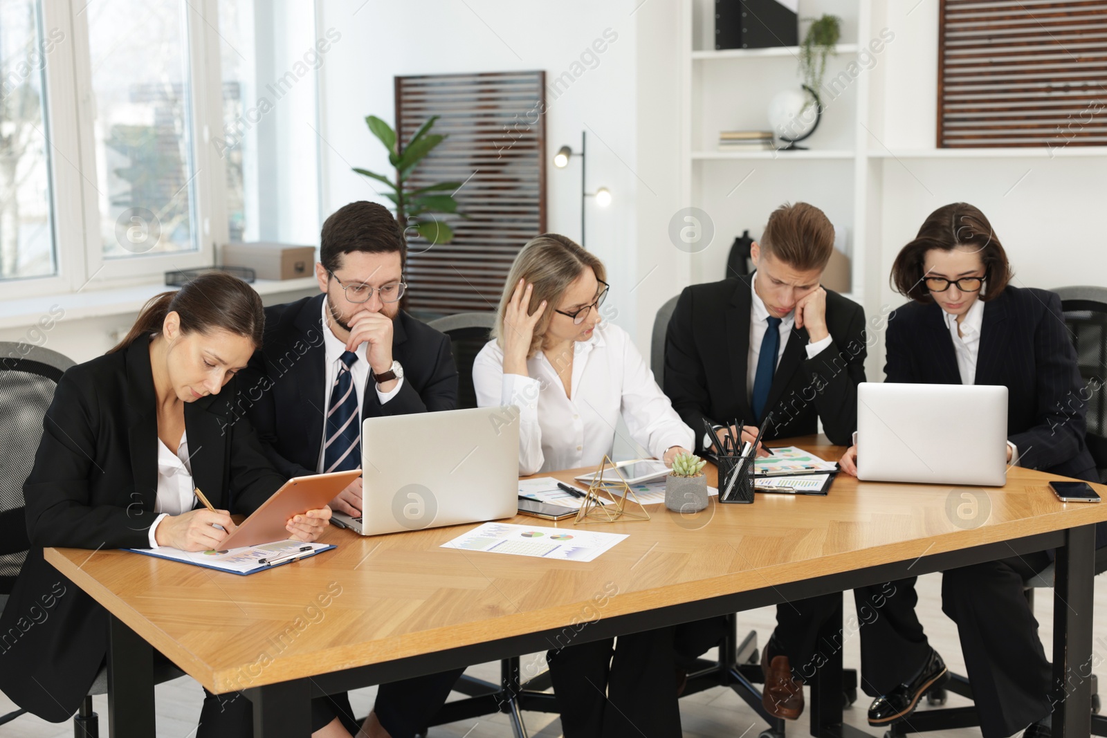 Photo of Coworkers with different devices working together at wooden table in office