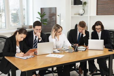 Coworkers with different devices working together at wooden table in office