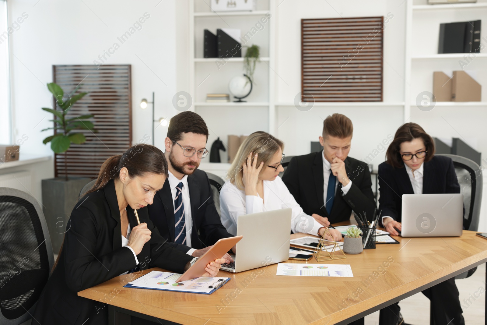 Photo of Coworkers with different devices working together at wooden table in office