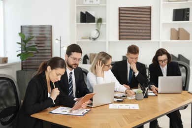 Coworkers with different devices working together at wooden table in office