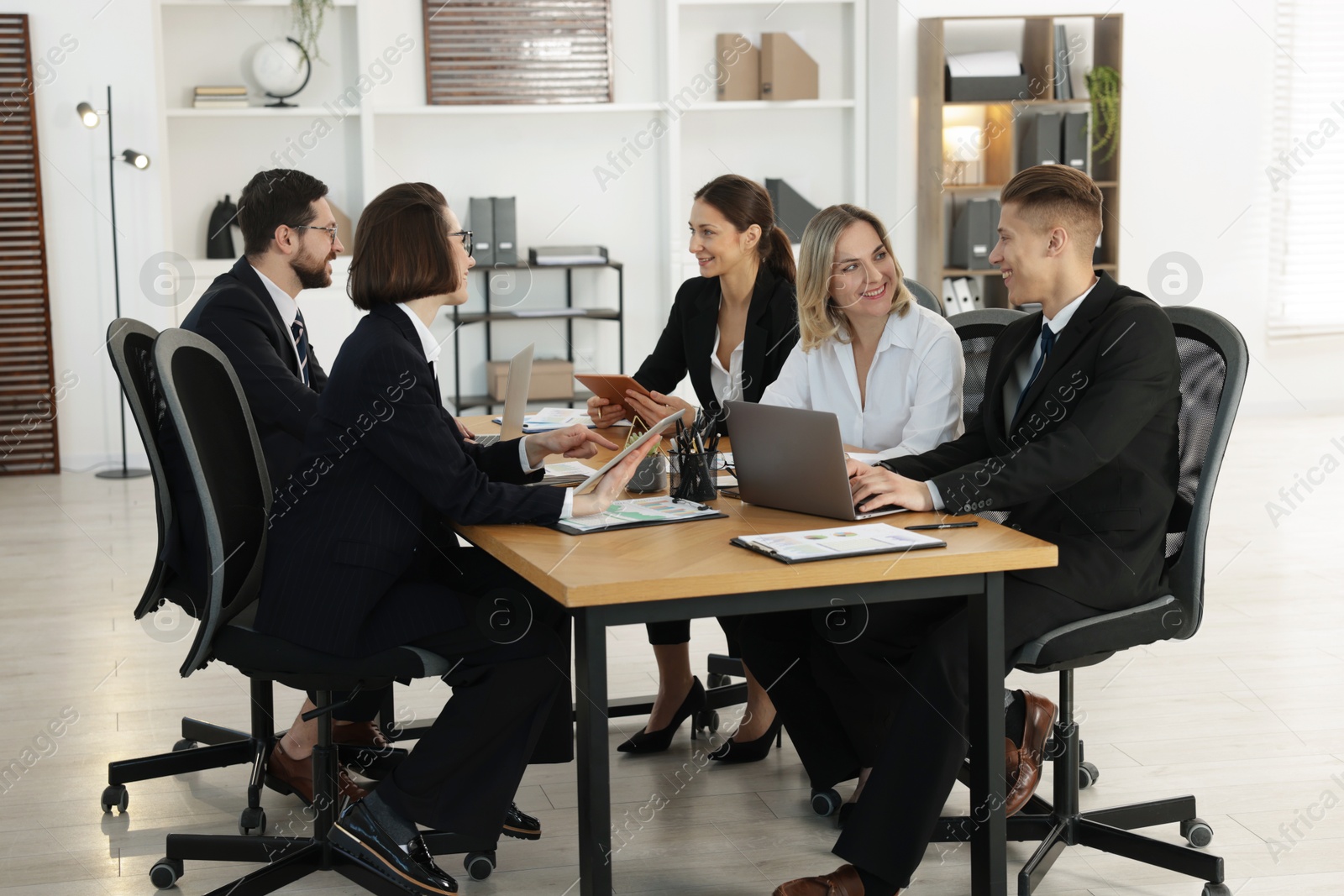 Photo of Coworkers with different devices working together at wooden table in office