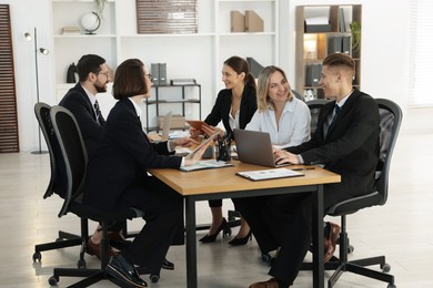 Photo of Coworkers with different devices working together at wooden table in office