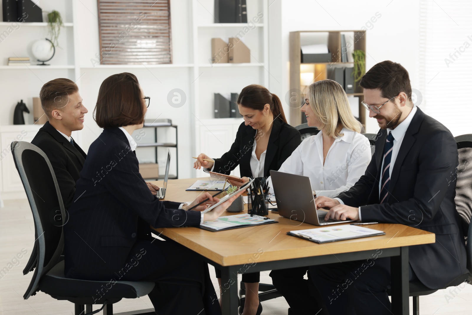 Photo of Coworkers with different devices working together at wooden table in office