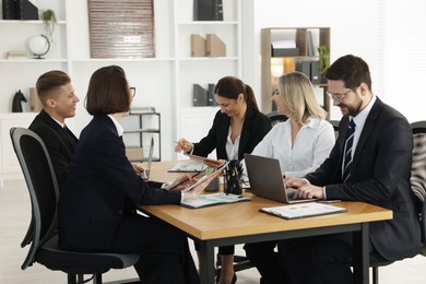 Photo of Coworkers with different devices working together at wooden table in office