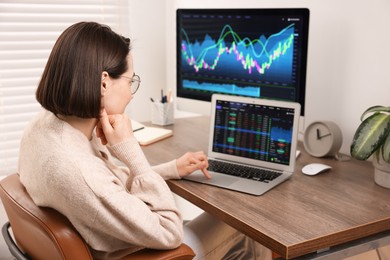 Photo of Stock exchange. Woman analysing financial market on laptop at wooden table indoors