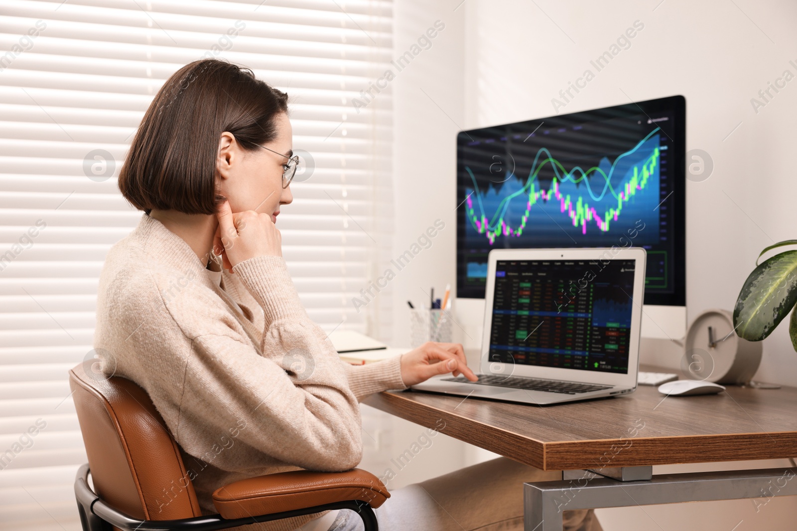 Photo of Stock exchange. Woman analysing financial market on laptop at wooden table indoors