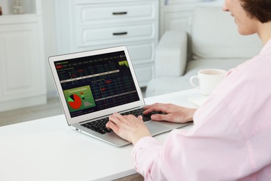 Photo of Stock exchange. Woman analysing financial market on laptop at white table indoors, closeup