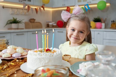 Cute little girl at table with birthday cake and different treats indoors. Surprise party