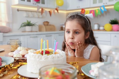 Photo of Cute little girl blowing out candles on birthday cake indoors. Surprise party