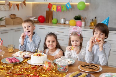 Children at table with tasty cake and different treats indoors. Surprise party