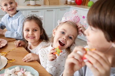 Photo of Children with treats at table indoors. Birthday surprise party