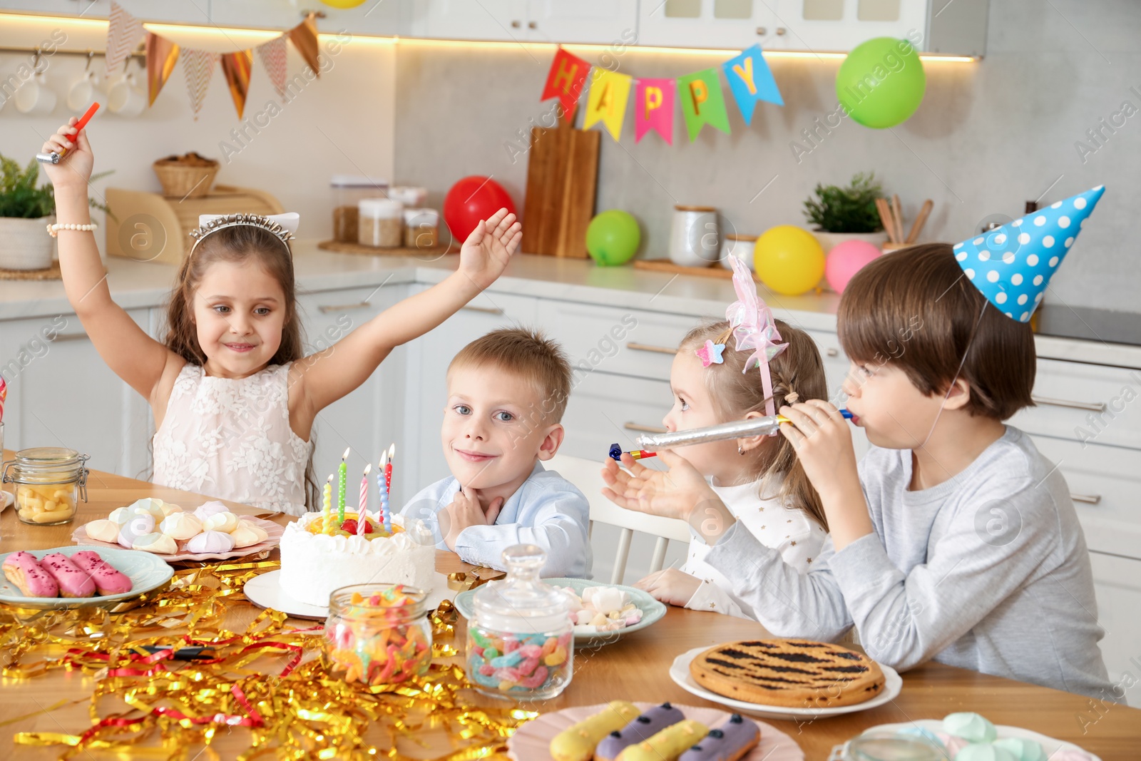 Photo of Children at table with tasty cake and different treats indoors. Surprise party