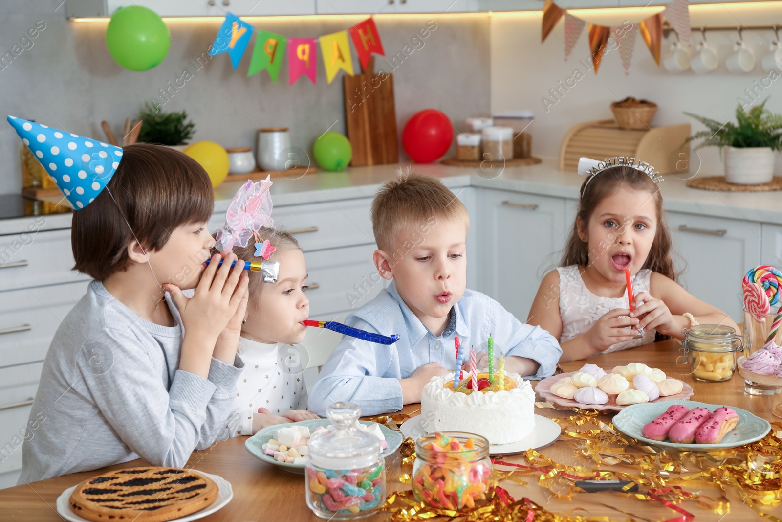 Photo of Children at table with tasty cake and different treats indoors. Surprise party