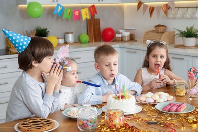 Children at table with tasty cake and different treats indoors. Surprise party