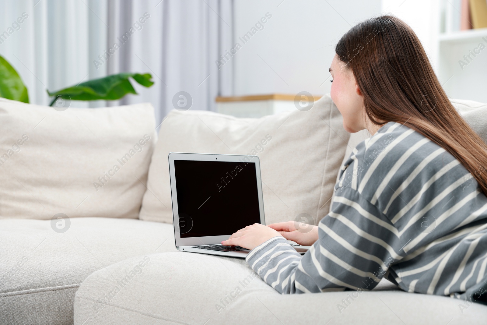 Photo of Young woman using laptop on sofa at home. Space for text