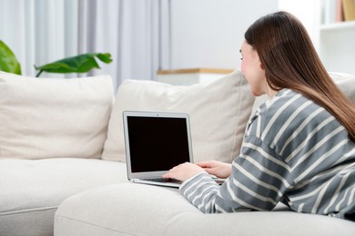 Young woman using laptop on sofa at home. Space for text