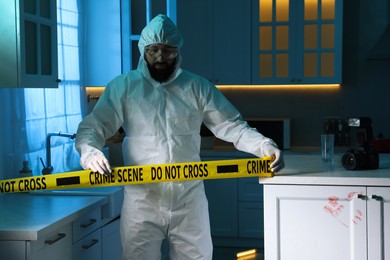 Forensic expert blocking way to crime scene with yellow tape indoors