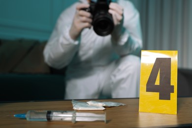 Forensic expert with camera working at crime scene indoors, focus on drugs and numbered marker stand