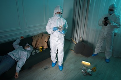 Forensic experts working at crime scene with dead woman's body indoors