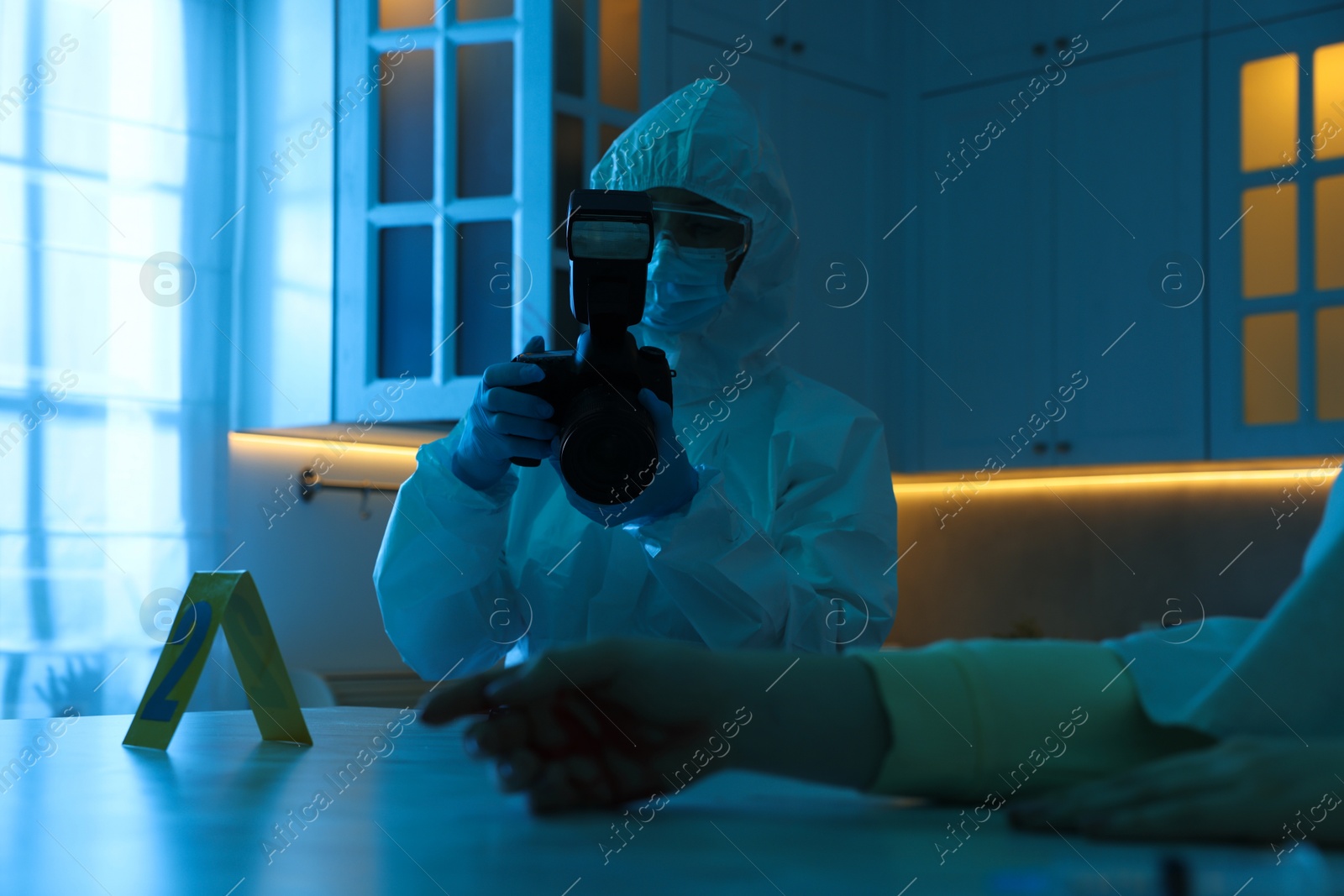 Photo of Forensic expert with camera working at crime scene and dead woman's body indoors, closeup