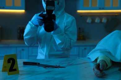 Forensic expert with camera working at crime scene and dead woman's body indoors, closeup