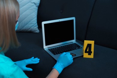 Photo of Forensic expert taking fingerprints with brush from laptop at crime scene