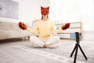 Quadrobics. Woman in fox mask and gloves recording video at home