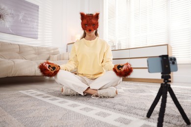 Photo of Quadrobics. Woman in fox mask and gloves recording video at home