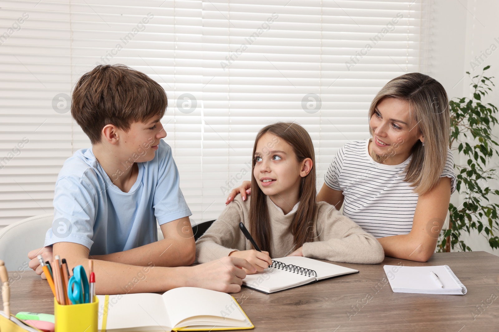 Photo of Smiling mother helping her children with homework at table indoors