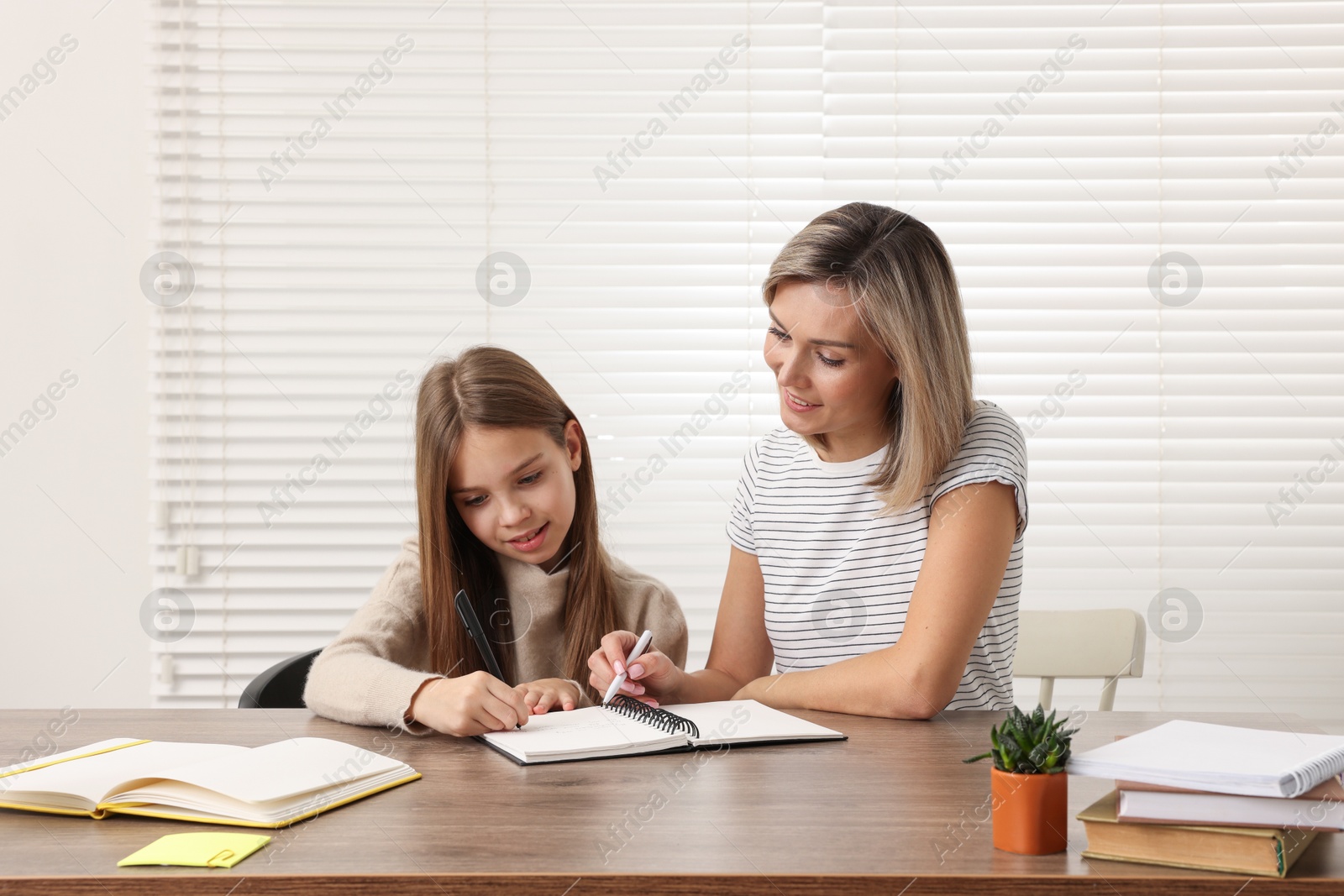 Photo of Smiling mother helping her daughter with homework at table indoors