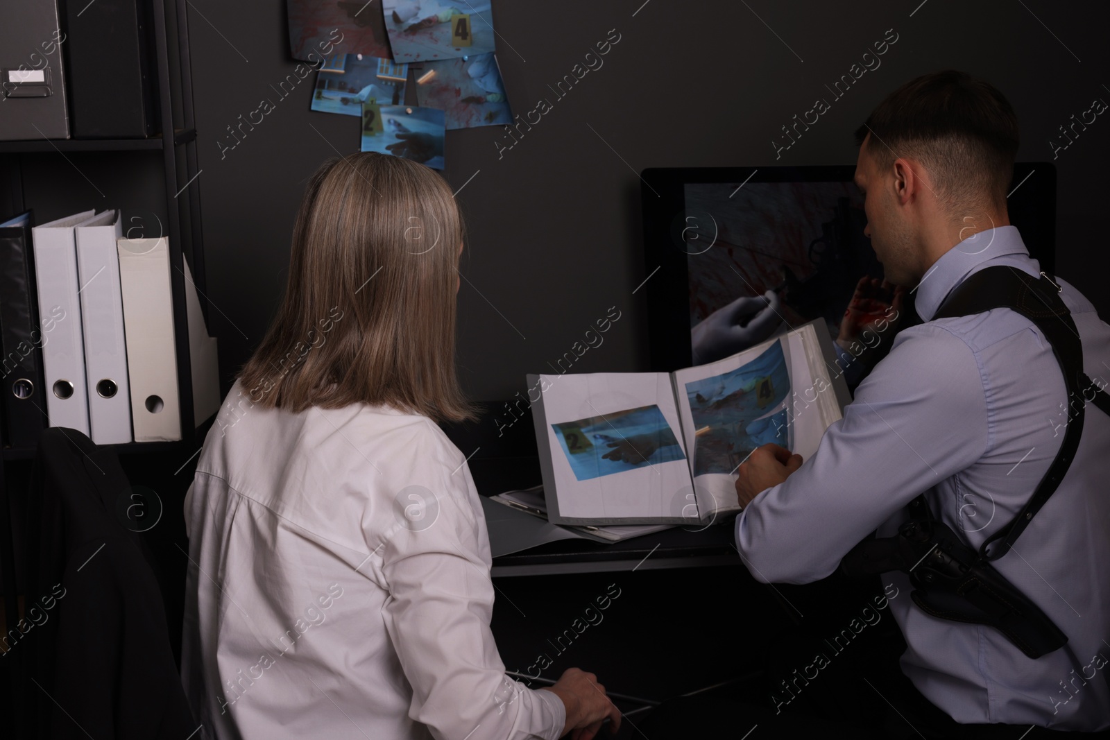 Photo of Forensic experts working with crime scene photos in office, back view